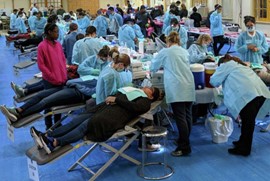 Dental providers treat patients in mobile chairs arranged in long lines on the floor of a convention center