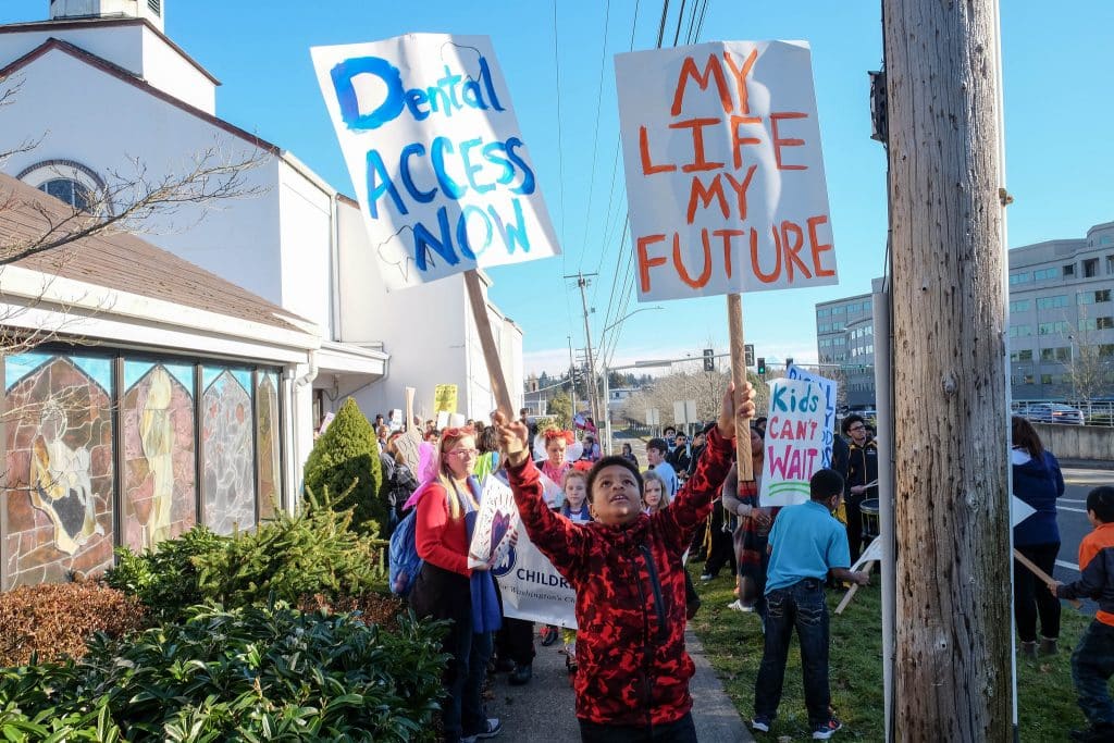 young kid holding "dental access now" and "My life, My future" signs