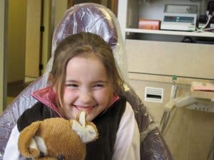 little girl smiling in dental chair holding teddy bear